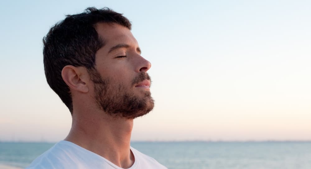 man in front of ocean with eyes closed